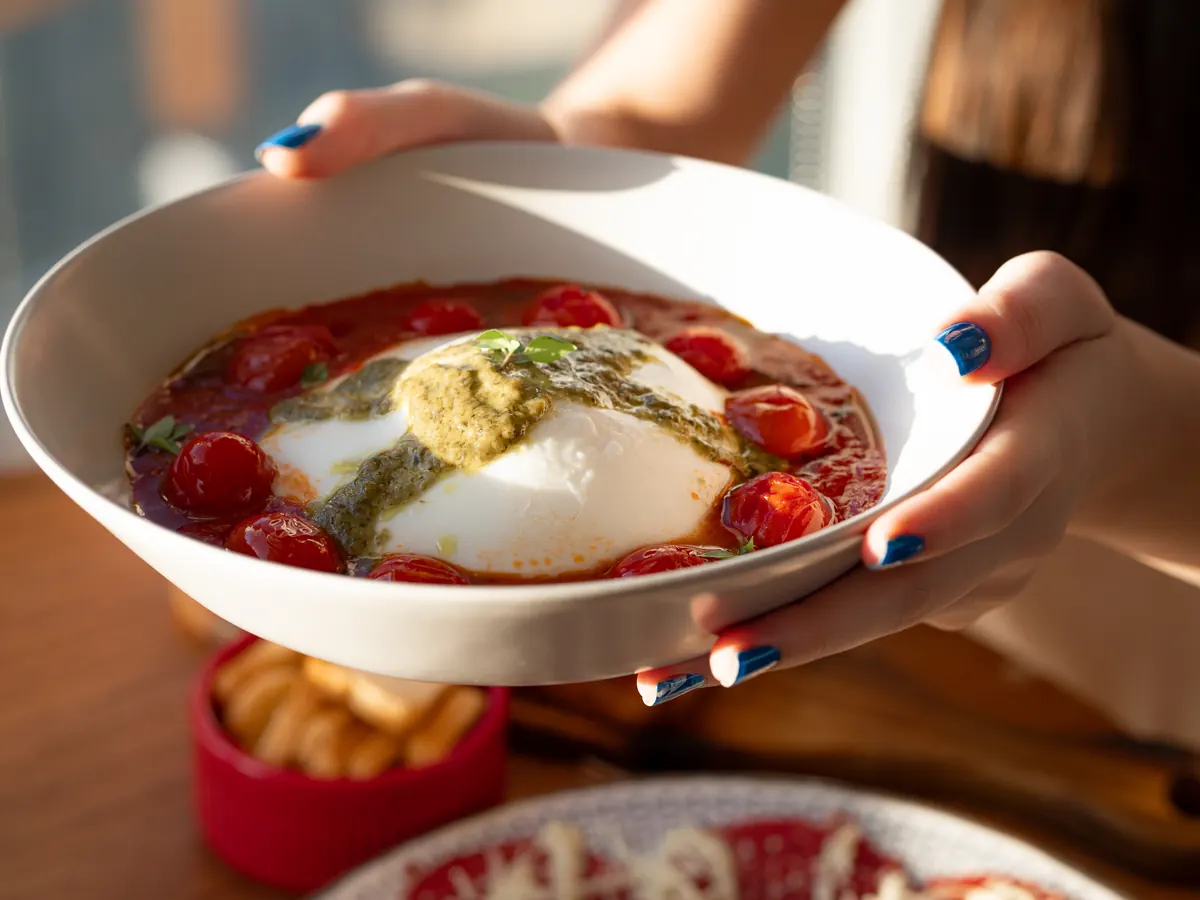 Prato de burrata com pesto de ervas e tomate confit, servido à mesa